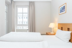 A hotel room with a bed, a nightstand with a lamp, a window with curtains, and a framed picture on the wall. - Komfortable Ferienwohnung im Seepark Sellin (Sellin)