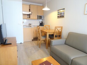 A compact living space with a kitchenette, a dining area with wooden furniture, a sofa, and a television on a wooden table. - Komfortable Ferienwohnung im Seepark Sellin (Sellin)