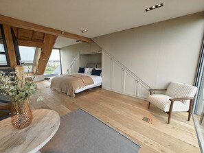 A bedroom with a bed, a chair, a wooden table with a vase, and a view through a window. - 5 Bed in Blyth (oc-t34727) (Blyth)