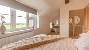 Ett sovrum med ett stort fönster, en säng med ett mönstrat överkast, ett sängbord och en spegel.