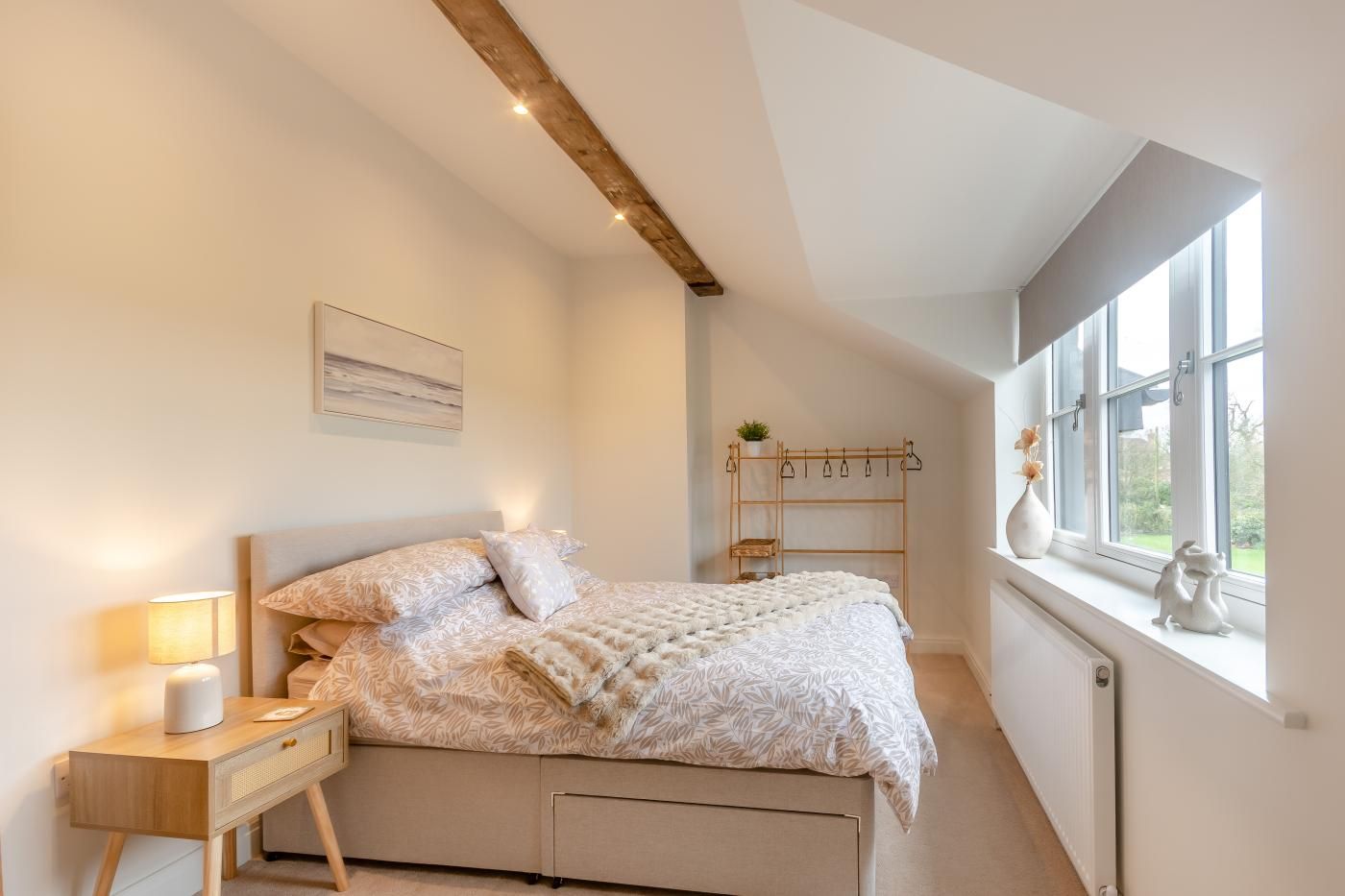 A bedroom with a bed, bedside table, lamp, window, and a wooden shelf with plants.