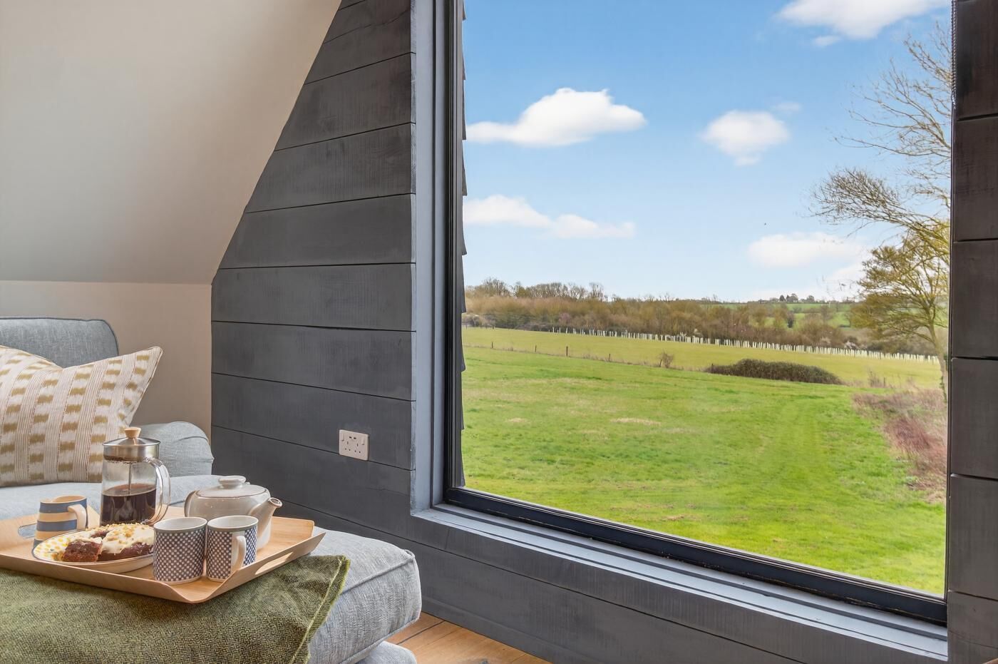 Une chambre avec une grande fenêtre, un lit, un plateau avec des articles pour le petit-déjeuner et une vue sur un champ verdoyant.