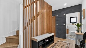 Un interior modern amb una escala, una separació de fusta, una cadira amb espai d'emmagatzematge, una catifa estampada i una planta petita.