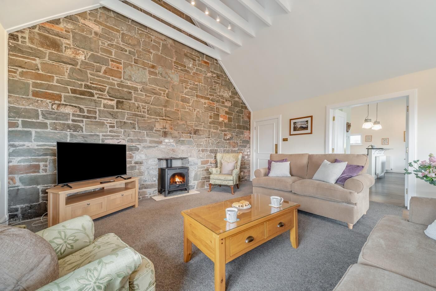 A cozy living room with a stone wall, a fireplace, a television, a sofa, and a coffee table.