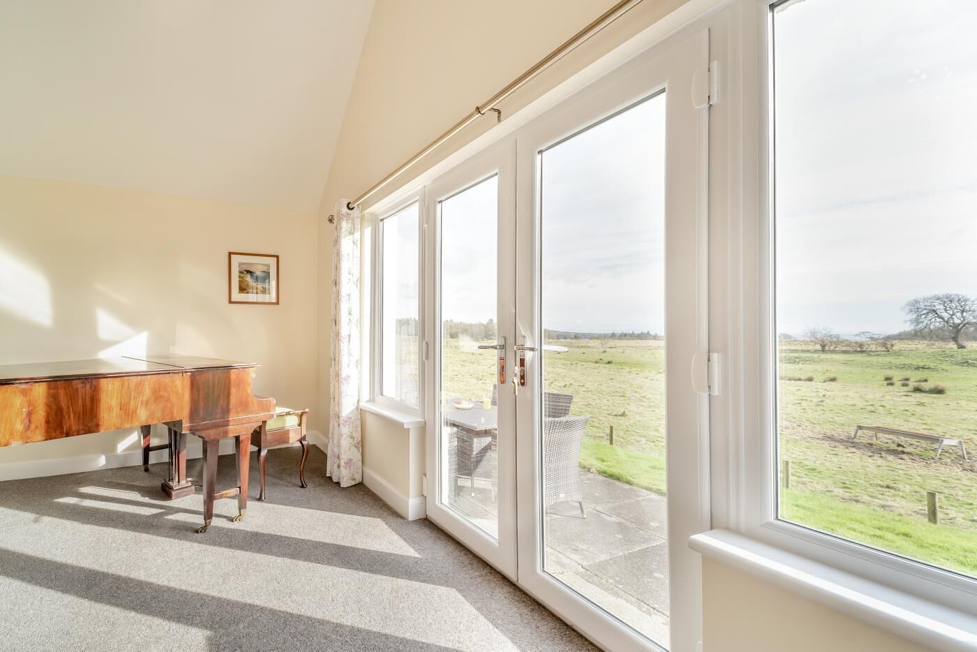 A room with a piano, large windows, and a view of a grassy field.