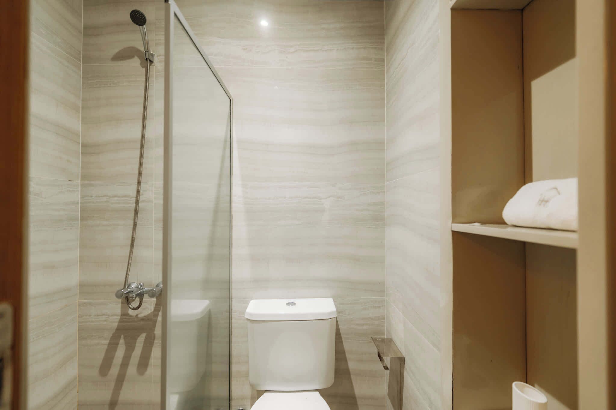 Un baño con ducha, inodoro y una estantería con toalla.