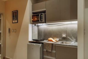 A compact kitchen with a microwave, a small refrigerator, a sink, and a marble backsplash. - Hestia en Cochabamba Boutique (Buenos Aires)
