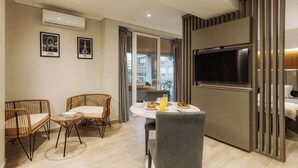 A modern living room with a flat-screen TV, wicker furniture, a dining table with breakfast, and a balcony view. - Hestia en Cochabamba Boutique (Buenos Aires)