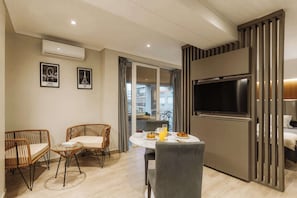 Una sala moderna con un televisor de pantalla plana, muebles de mimbre, una mesa de comedor con desayuno y vistas a un balcón.