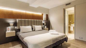 A modern hotel room with a large bed, bedside lamps, a wooden headboard, and a visible bathroom door.