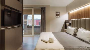 Habitación de hotel con cama, televisión, puerta corrediza de vidrio que da a un balcón y un cuadro en la pared.