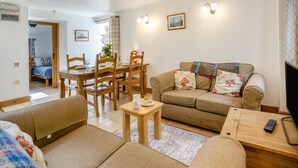 Ein Wohnzimmer mit einer Couch, einem Esstisch mit Stühlen, einem Fernseher und einer Fernbedienung.