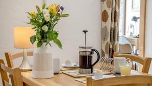 Una mesa de madera con una cafetera, un jarrón con flores, una lámpara y una taza.
