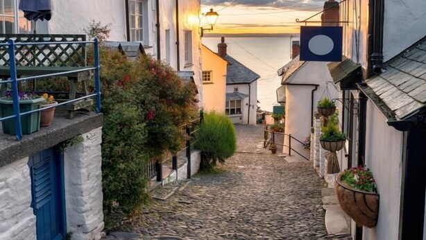 A narrow cobblestone street with buildings on either side, a blue door, and a hanging flower pot. - 2 Bed in Hartland (oc-d35028) (Hartland)