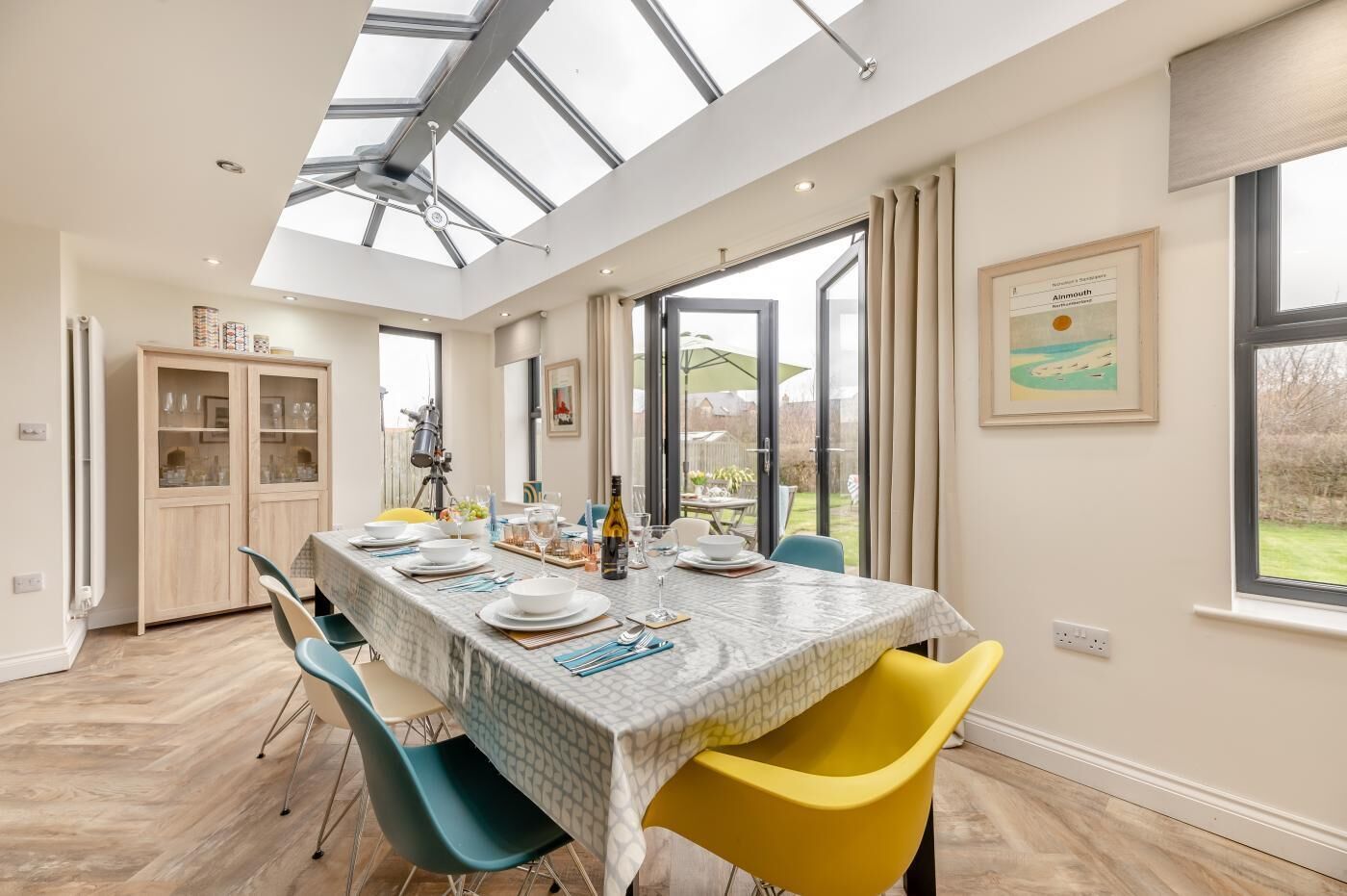 Un espace repas avec une table dressée pour quatre personnes, un plafond haut doté d’une verrière et une vue sur l’extérieur.
