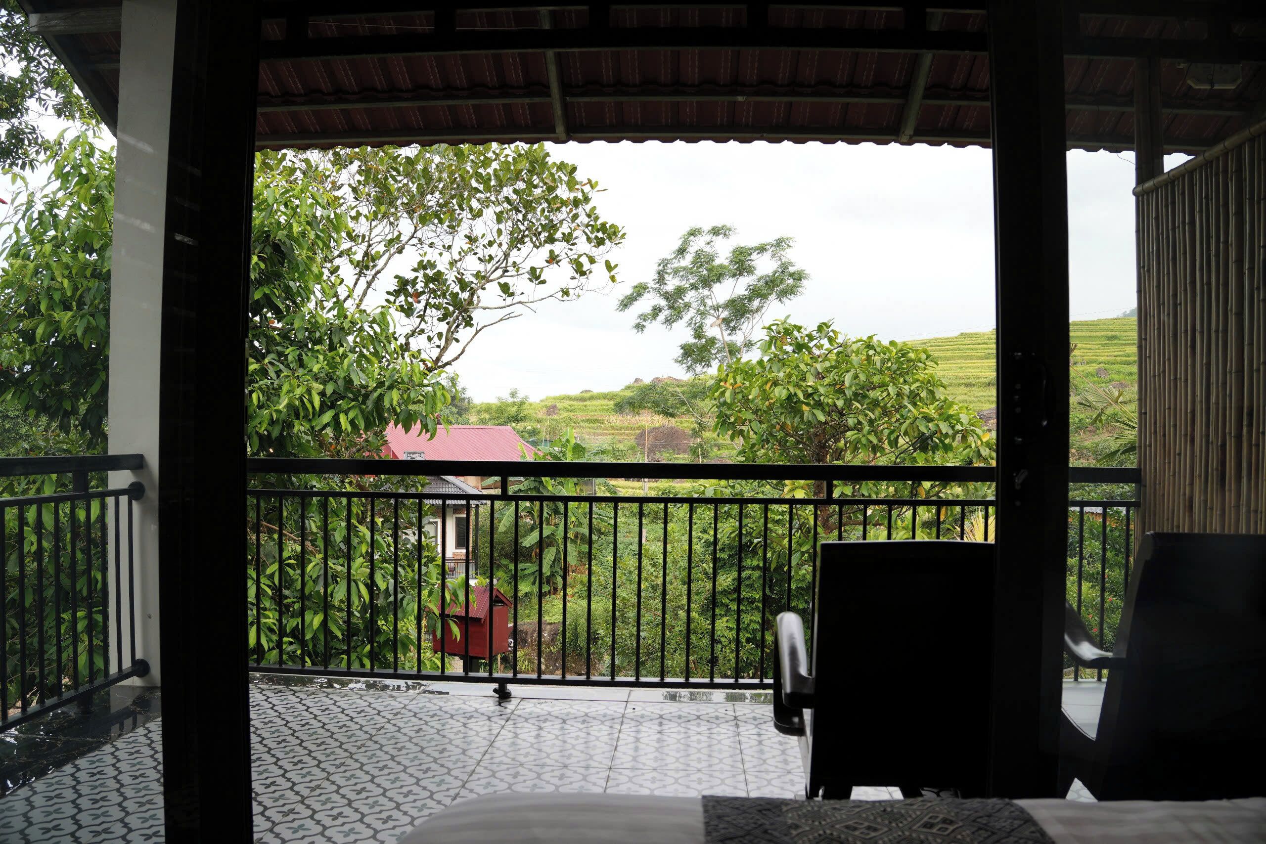 A balcony with a view of a green landscape and a red-roofed building.