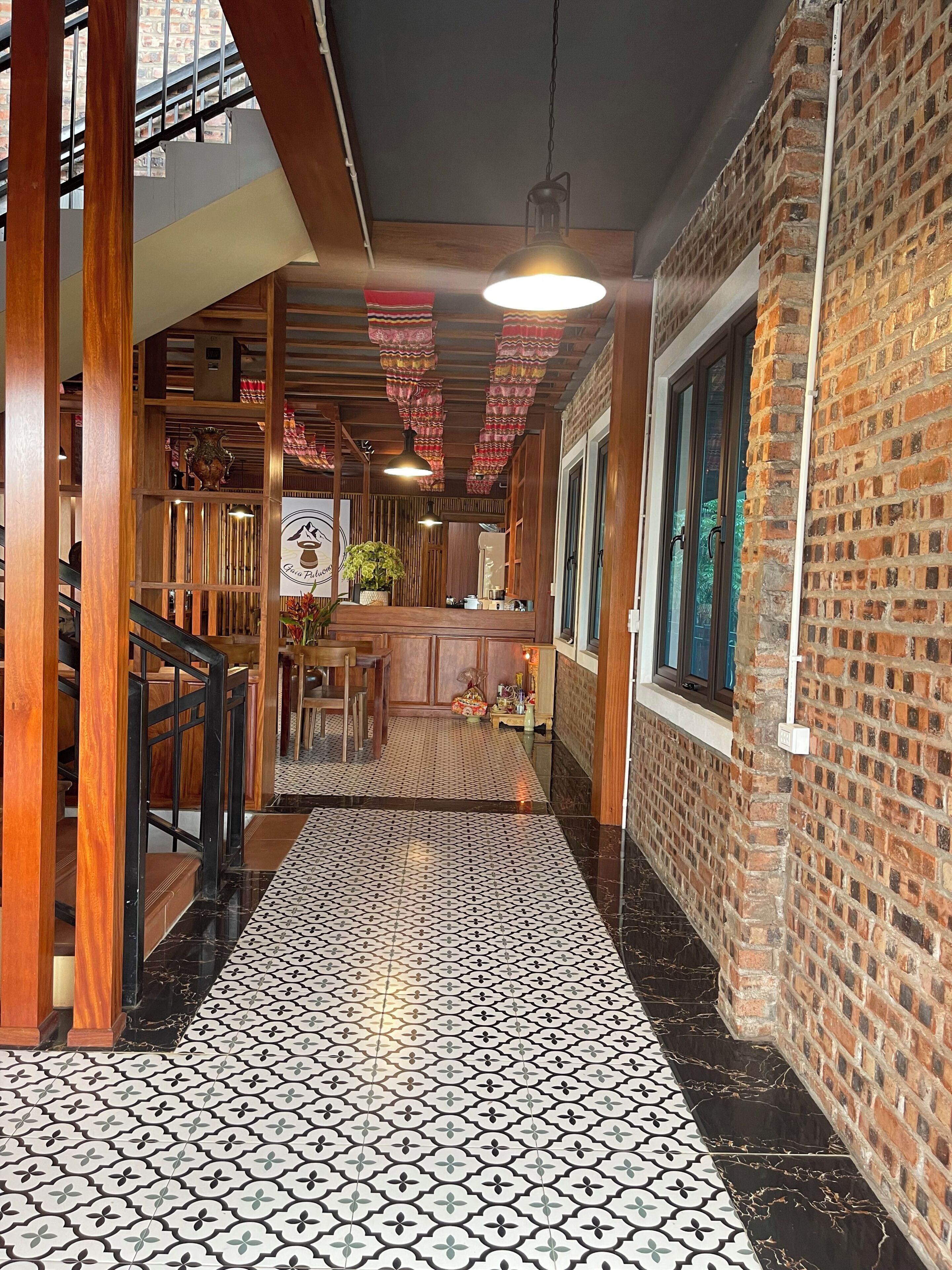A corridor with patterned flooring, wooden railings, and a brick wall.