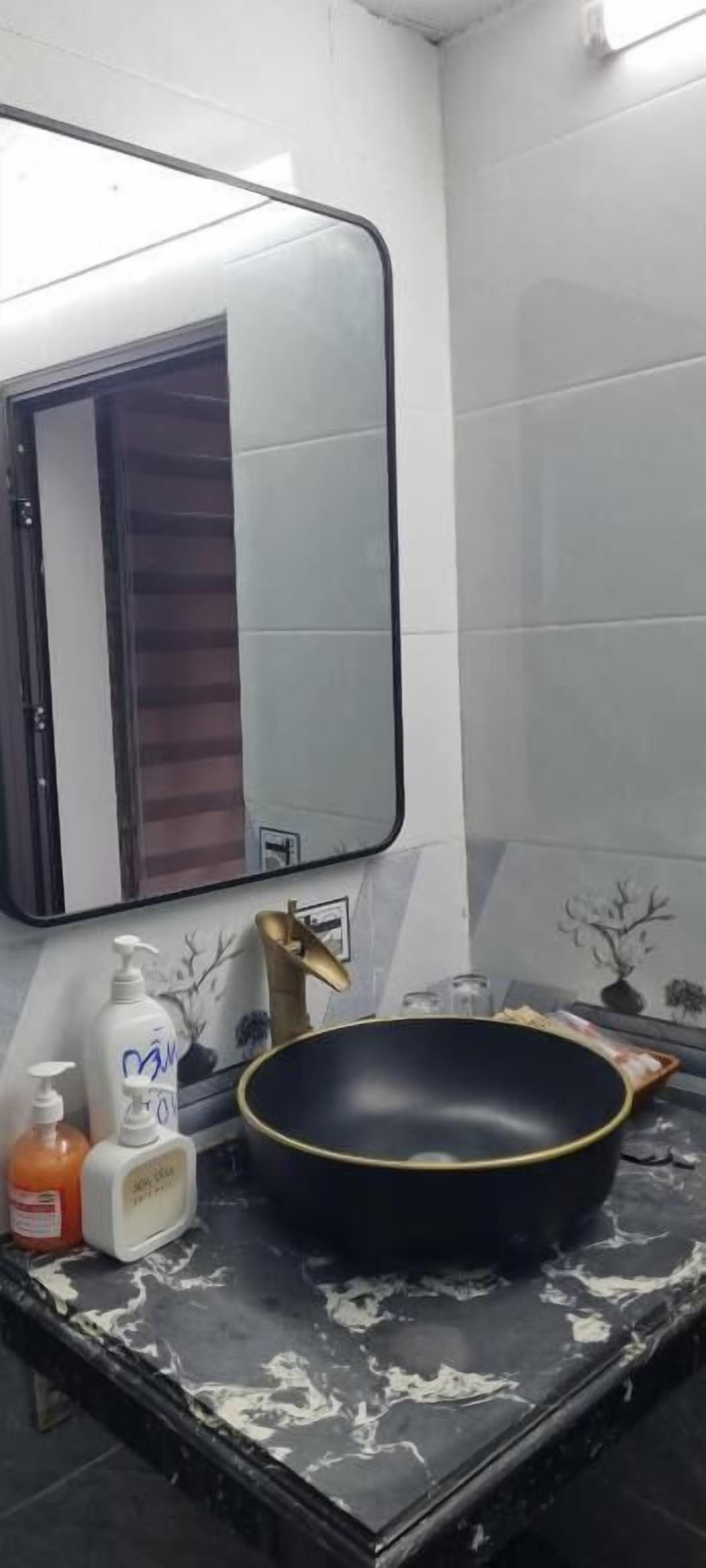 A bathroom with a black sink, white tiles, a mirror, and toiletries.