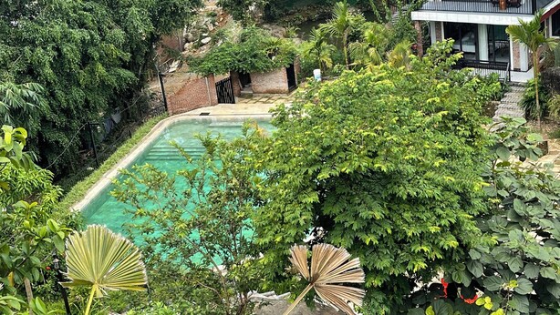 Una casa con piscina, rodeada de vegetación exuberante y montañas al fondo.