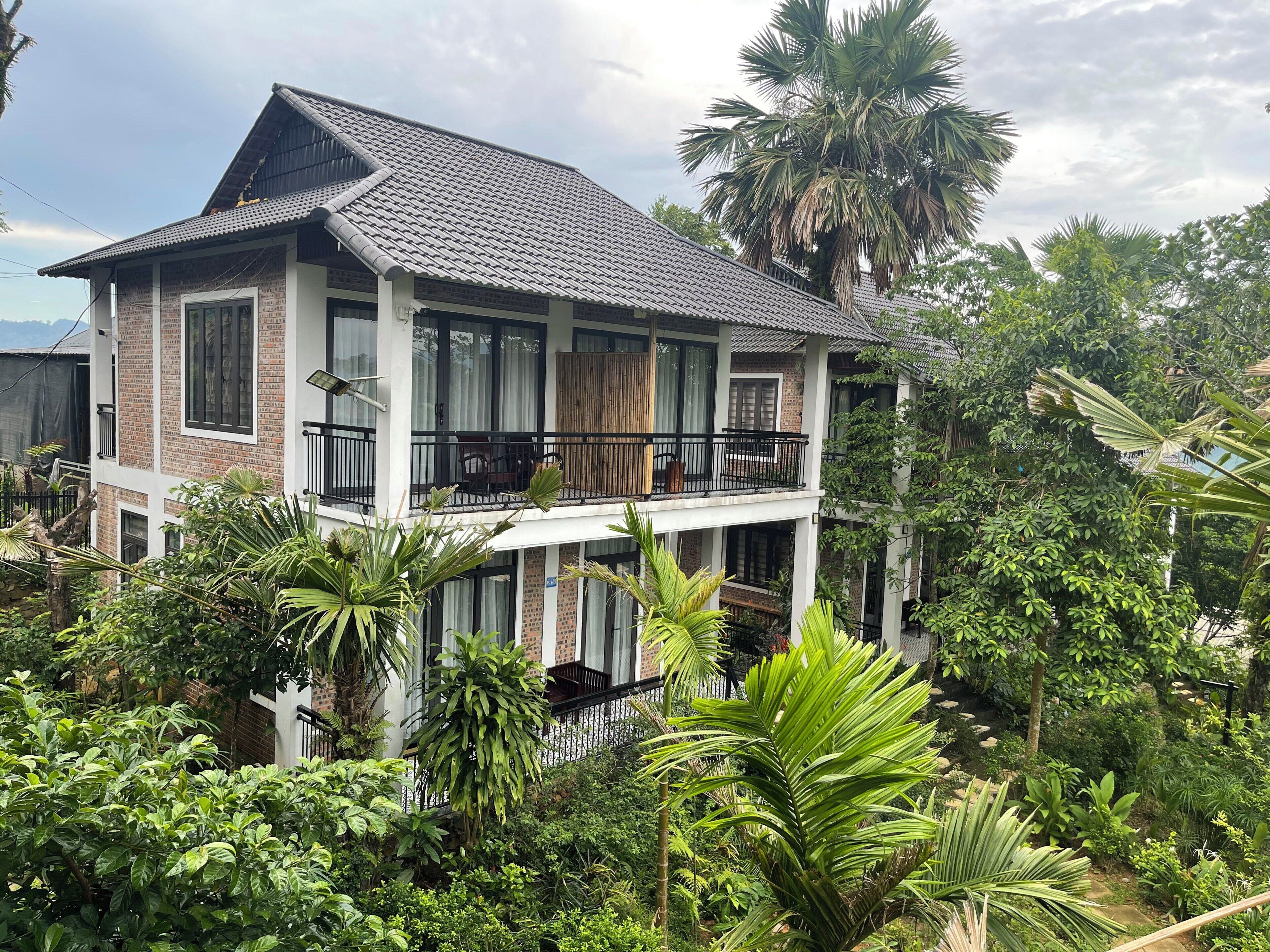 A multi-story building with a balcony, surrounded by lush greenery.