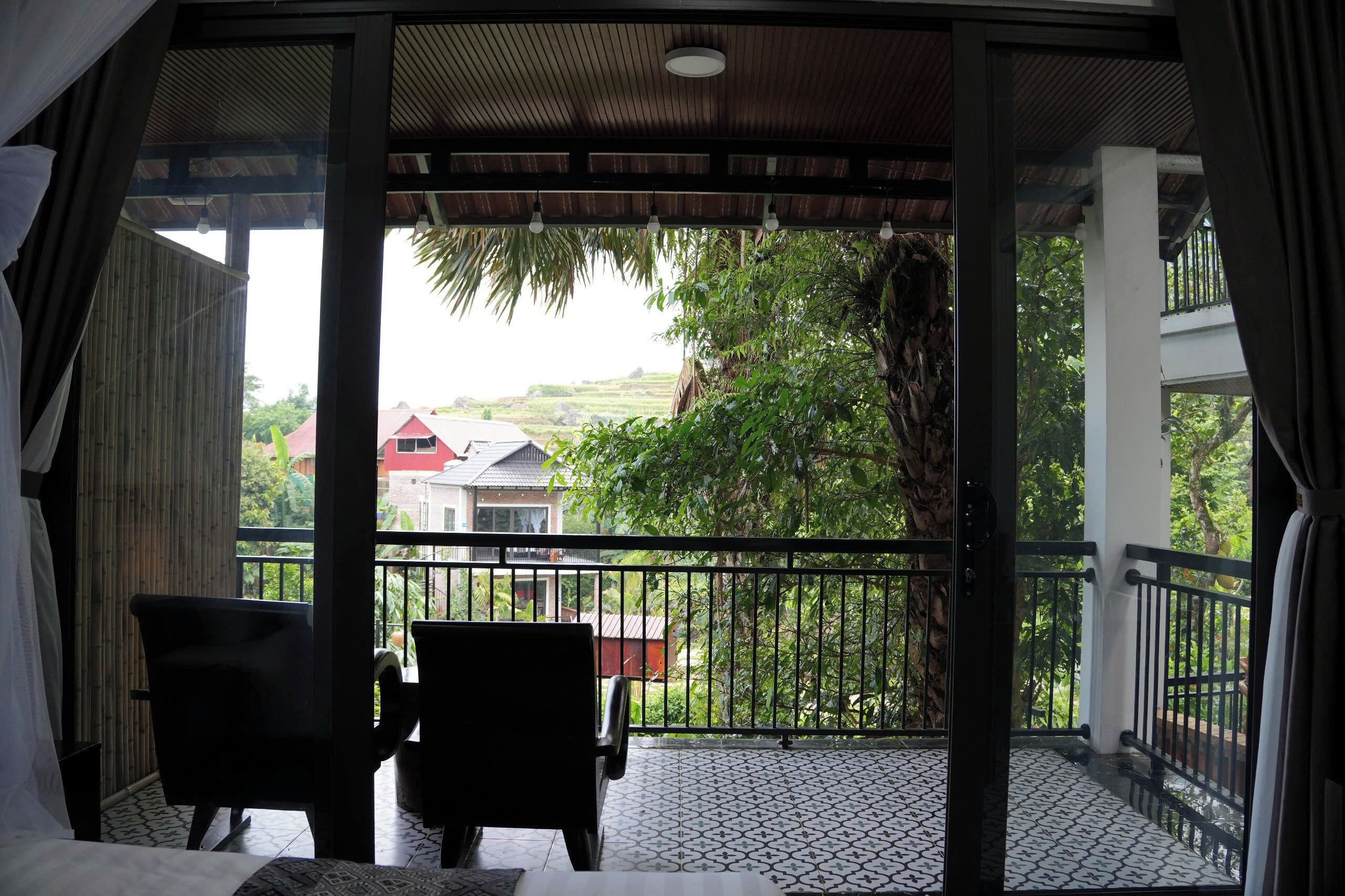 A balcony with two chairs, a table, and a view of a house and greenery.