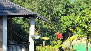 Una casa con balcón, rodeada de abundante vegetación y montañas al fondo.