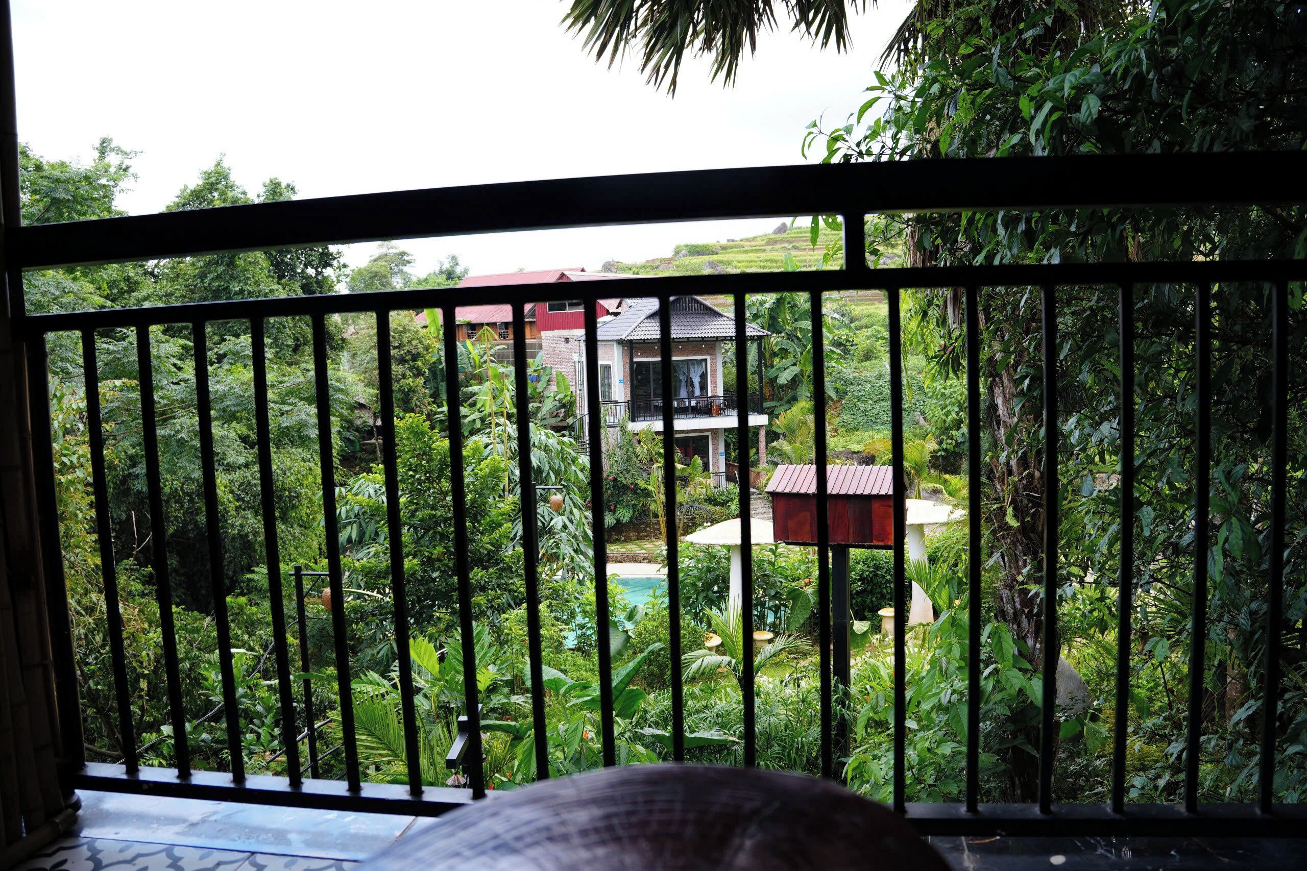 Un balcon donnant sur un jardin luxuriant, avec une maison en arrière-plan.