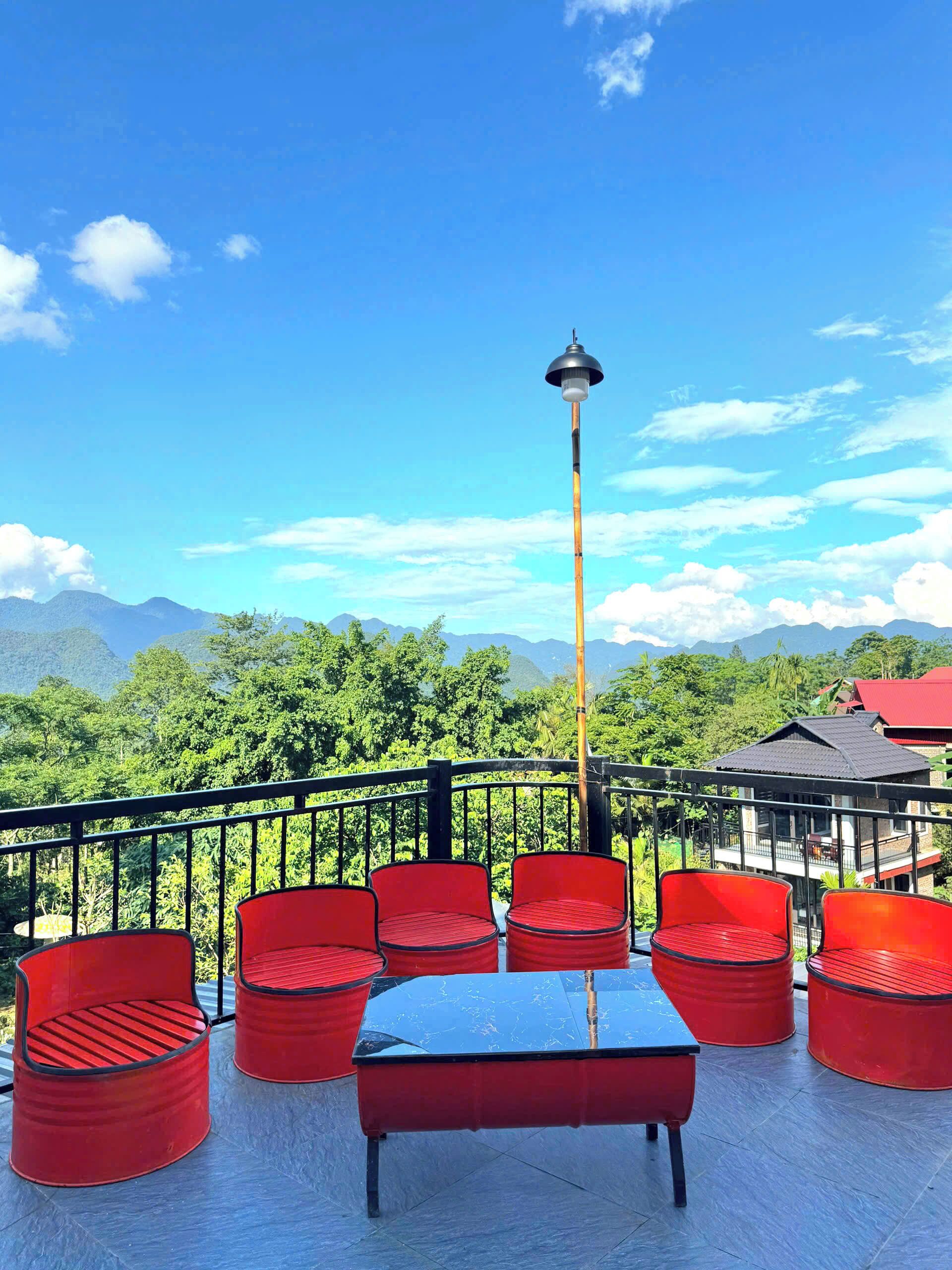 A terrace with red chairs and a table, overlooking a mountainous landscape.