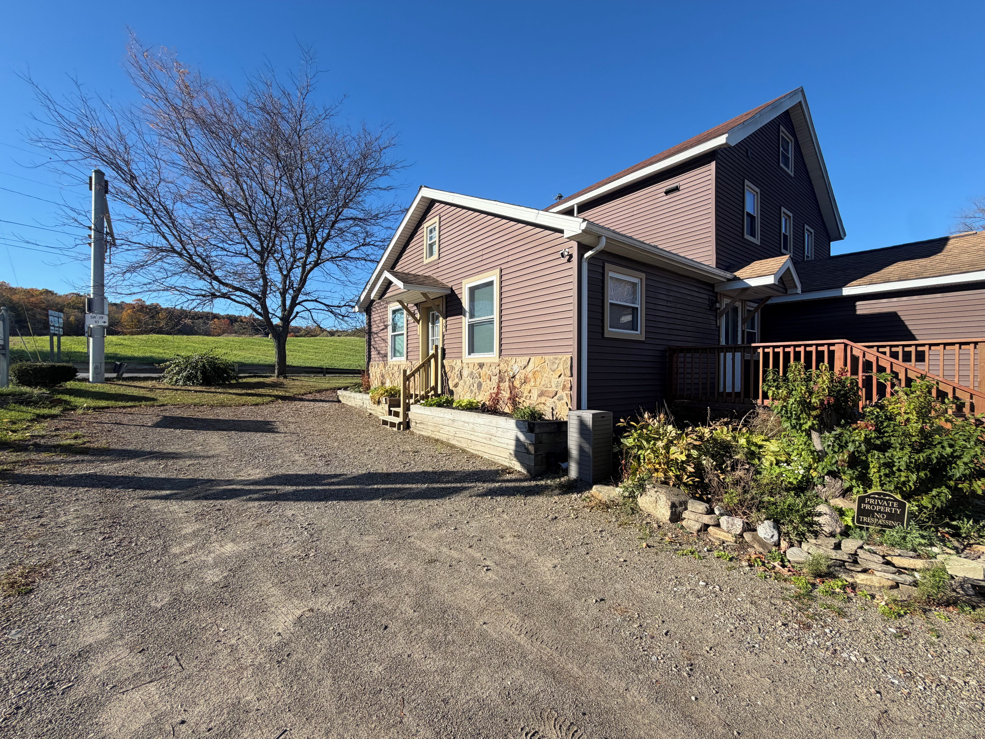 A two-story house with a stone foundation, a gravel driveway, and a wooden fence.