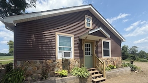 A single-story house with a stone foundation, a front porch with steps, and a small window above the door. - Cozy Creek Retreat - Spiral staircase,AC,high speed WiFi (Waterford)
