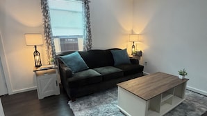 A modern living room with a dark sofa, two side tables with lamps, a wooden coffee table, and a fluffy rug. - Cozy Creek Retreat - Spiral staircase,AC,high speed WiFi (Waterford)