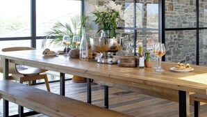 Una mesa de madera con bancos, un jarrón con flores y copas de vino.
