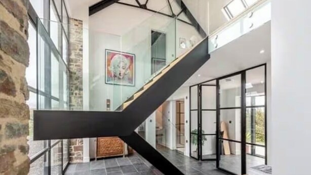 Un interior moderno con una escalera de cristal, paredes de piedra y un ventanal grande.