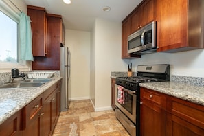 A kitchen with wooden cabinets, a stainless steel refrigerator, a microwave, a stove, and granite countertops. - Chula Vista Retreat Near Gaylord Pacific | 3BR/2BA (Chula Vista)