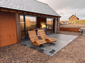 Um edifício moderno com fachada de pedra, grandes portas de correr de vidro e um deck de madeira com design de banco singular.