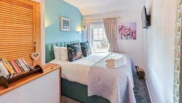 A bedroom with a bed, a bedside table with books, a window with curtains, and a wall-mounted TV.