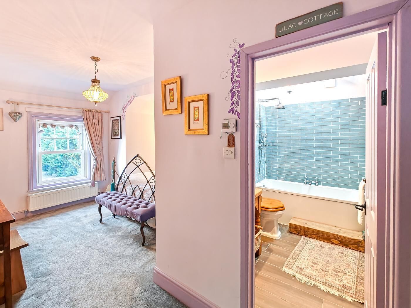 A room with a bed, a window with curtains, a wall-mounted heater, and a door leading to a bathroom with a blue-tiled shower.