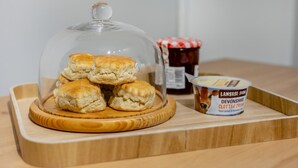 Ein Holztablett mit einer Glaskuppel, gefüllt mit Keksen, Marmeladenglas und Devonshire Clotted Cream.