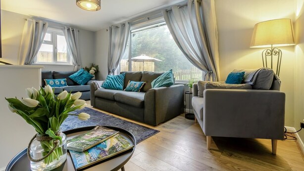 Ein modernes Wohnzimmer mit einer Sofagarnitur, einem Couchtisch mit Zeitschriften und einer Blumenvase.