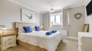 Una camera da letto con un letto, comodini, un termosifone, una finestra con tende e una televisione a parete, oltre a una decorazione a forma di cuore.