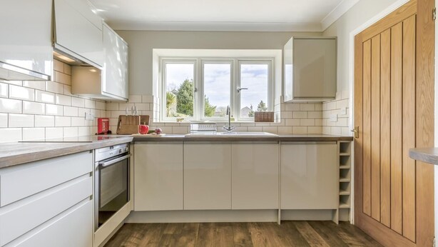 Una cucina moderna con mobili bianchi, pavimento in legno, una finestra con vista e forno integrato.