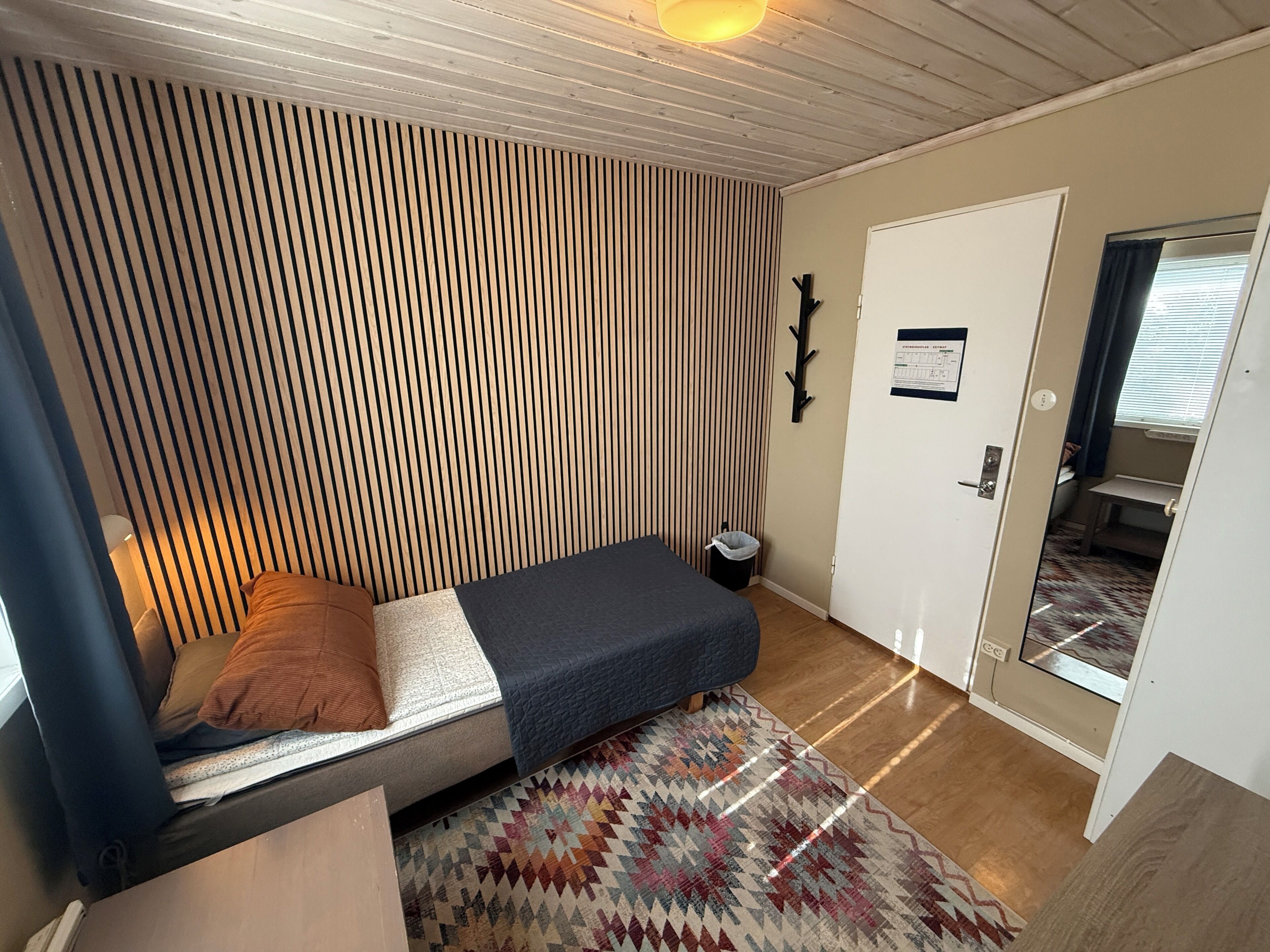A compact room with a bed, a patterned rug, a door, and a small window.