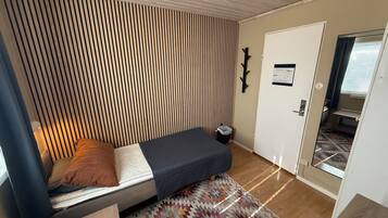 A compact room with a bed, a patterned rug, a door, and a small window.