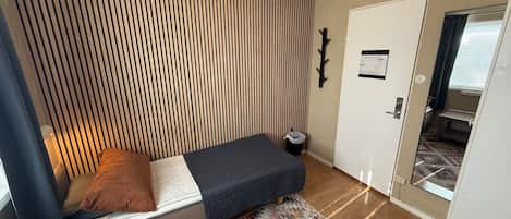 A compact room with a bed, a patterned rug, a door, and a small window.