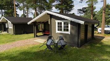 A small cabin with a porch and two chairs, surrounded by trees.