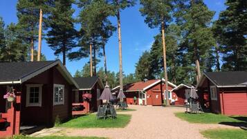 A row of red cabins with a gravel path leading to them, surrounded by tall trees.