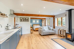 A modern kitchen with a large island, a cozy living area with a sofa and a fireplace, and a bedroom with a bed and a nightstand. - 1 Bed in Wheat Common (oc-c36015) (Richards Castle)