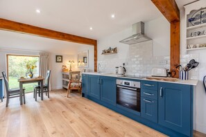 A modern kitchen with blue cabinets, a stainless steel range hood, and a dining area with a table and chairs. - 1 Bed in Wheat Common (oc-c36015) (Richards Castle)