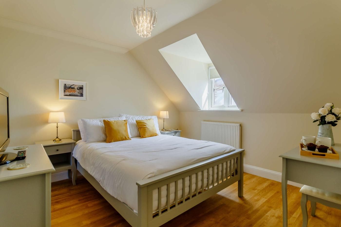 Une chambre à coucher comprenant un lit, des tables de chevet, une commode, un bureau, une chaise, une fenêtre et un lustre.