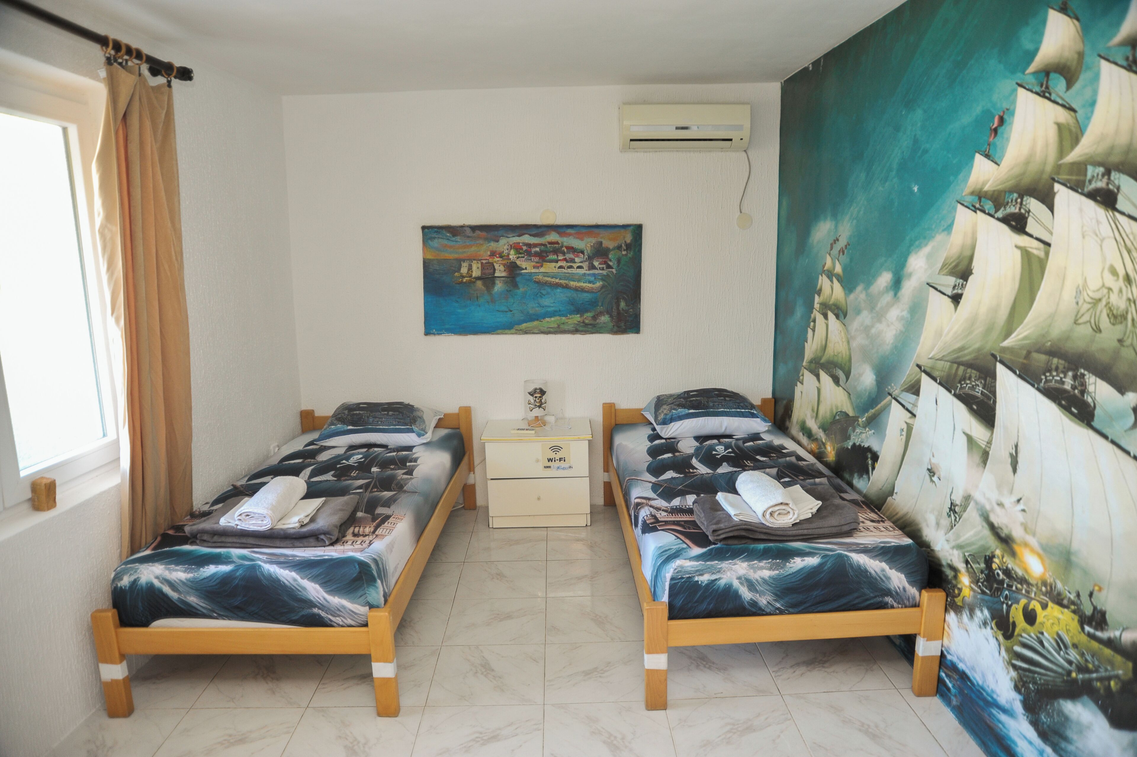 Quarto com duas camas de madeira, uma mesa de cabeceira, um quadro e um aparelho de ar condicionado.